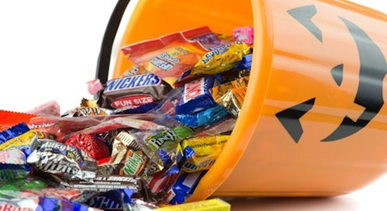 Halloween jack-o-lantern pail with spilling candy over white